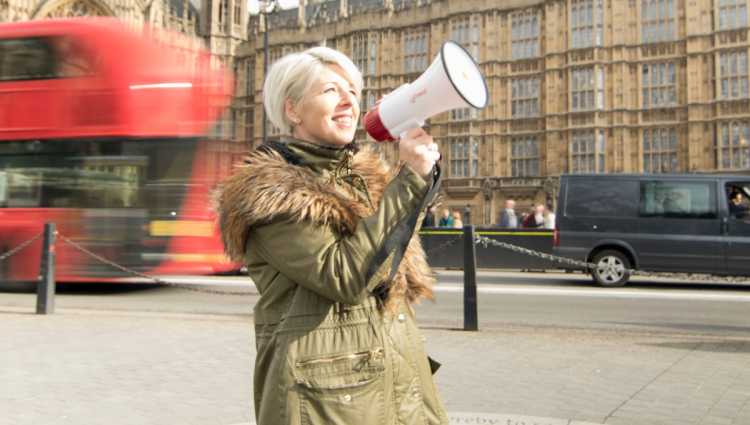 A woman stands near a busy London road with a megaphone