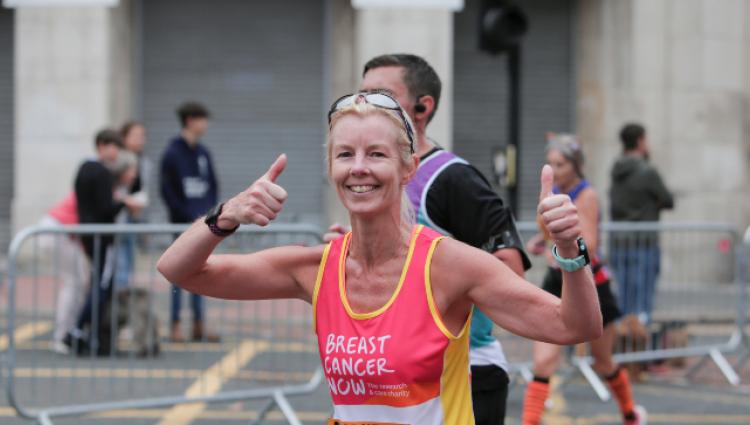 A smiling woman running along a city street wearing a pink Breast Cancer Now fundraising top